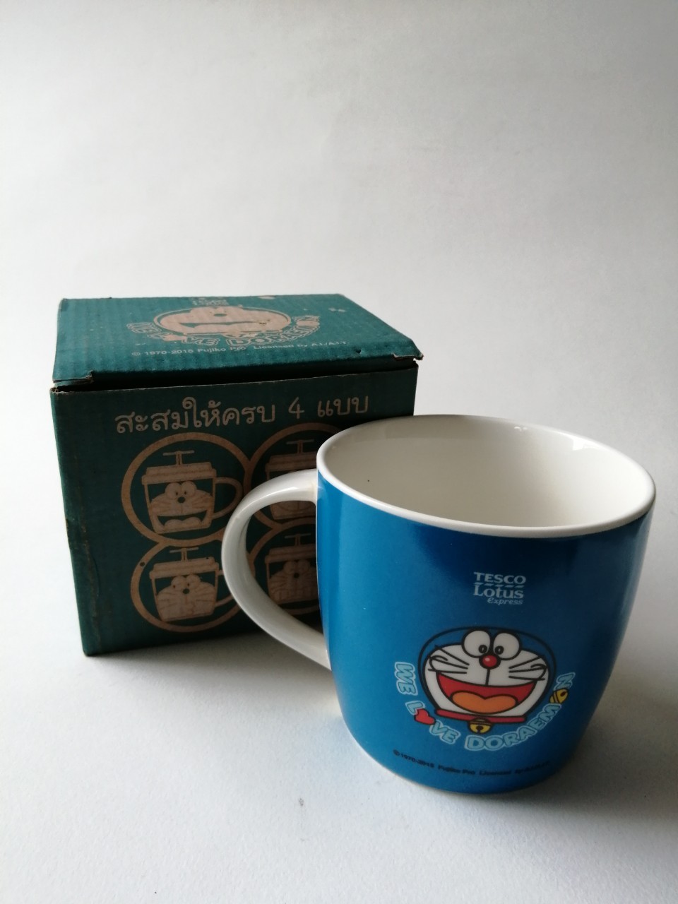 แก้วน้ำเซรามิก "แก้วโดราเอม่อน หน้ายิ้มแลบลิ้นด้านข้าง **ไม่มีฝายางสีน้ำเงิน พร้อมกล่อง" ของสะสมจากเทสโก้ โลตัส***สภาพสะสมเก่าเก็บ กล่องมีตำหนิตามภาพ