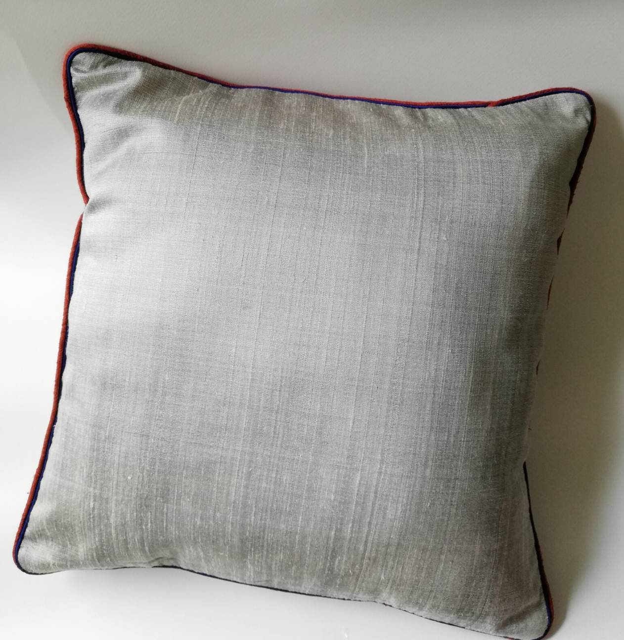 ปลอกหมอนอิงผ้าไหมไทยเท้2เส้น 16"*16" ของใหม่มีรอยเปื้อนเล็กน้อยตามภาพสุดท้าย เนื้อผ้าแบบมีเท็กเจอร์ เนื้อนุ่ม เย็น สีเทา แต่งกุ๊นขอบ2ชั้นด้วยสีแดงและสีน้ำเงิน ติดซิปซ่อน