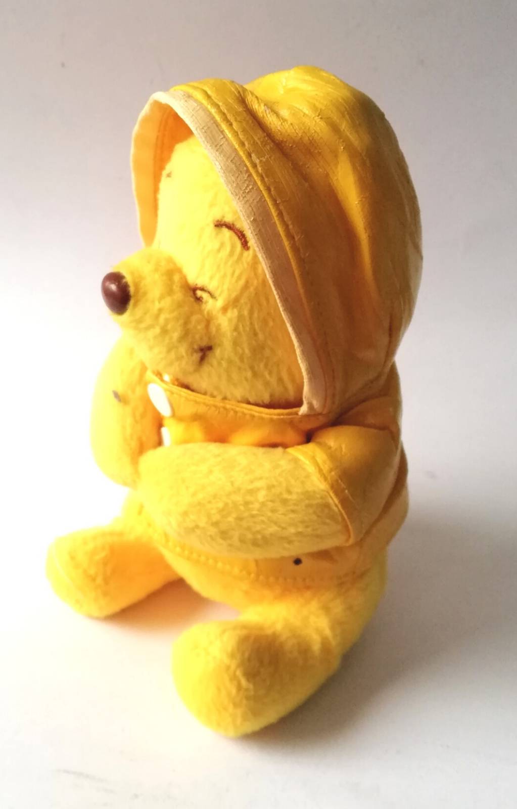 ตุ๊กตาผ้า Winnie the Pooh หมีพูห์สีเหลืองใส่เสื้อกันฝน ใต้หมวกมีลูกอ๊อดสีเขียว เสื้อเหลืองเป็นผ้าร่ม มีรอยแตกตามภาพ ขนาดประมาณ 5"