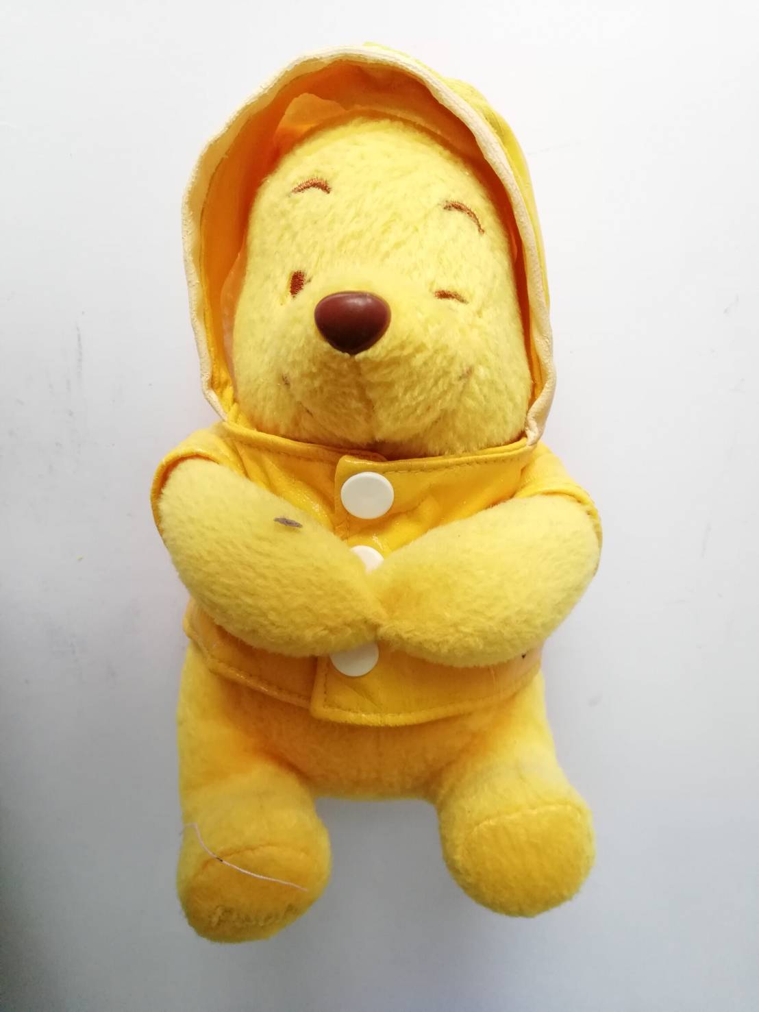 ตุ๊กตาผ้า Winnie the Pooh หมีพูห์สีเหลืองใส่เสื้อกันฝน ใต้หมวกมีลูกอ๊อดสีเขียว เสื้อเหลืองเป็นผ้าร่ม มีรอยแตกตามภาพ ขนาดประมาณ 5"