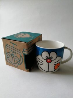 แก้วน้ำเซรามิก "แก้วโดราเอม่อน หน้ายิ้มแลบลิ้นด้านข้าง **ไม่มีฝายางสีน้ำเงิน พร้อมกล่อง" ของสะสมจากเทสโก้ โลตัส***สภาพสะสมเก่าเก็บ กล่องมีตำหนิตามภาพ